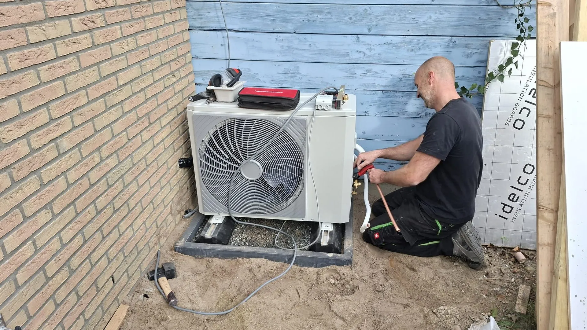 Monteur van Orivion sluit koelleidingen aan op een buitenunit naast een woning